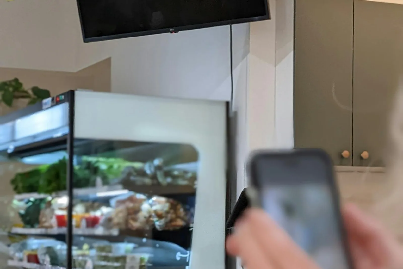 A shopper holding a phone near a refrigerated fresh food display